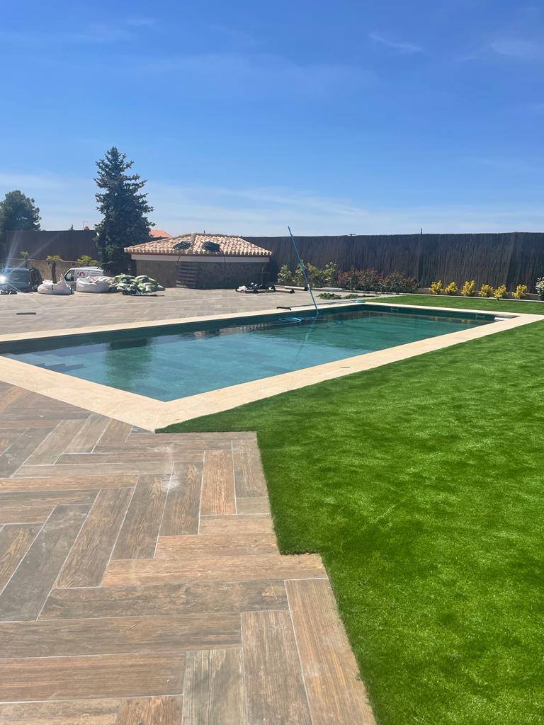 Piscina revestida en mosaico verde esmeralda con corona clara y solárium en porcelánico madera