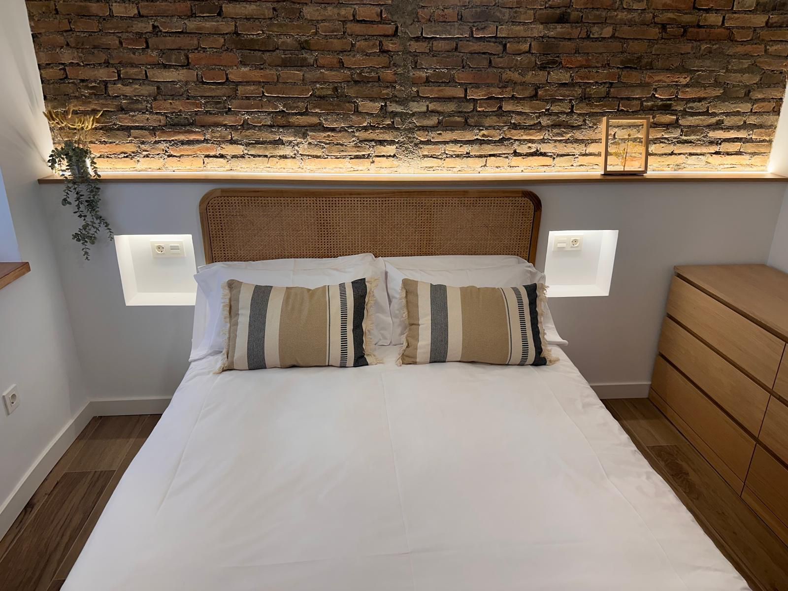 Dormitorio de diseño con pared de ladrillo visto iluminada y suelo porcelánico efecto madera