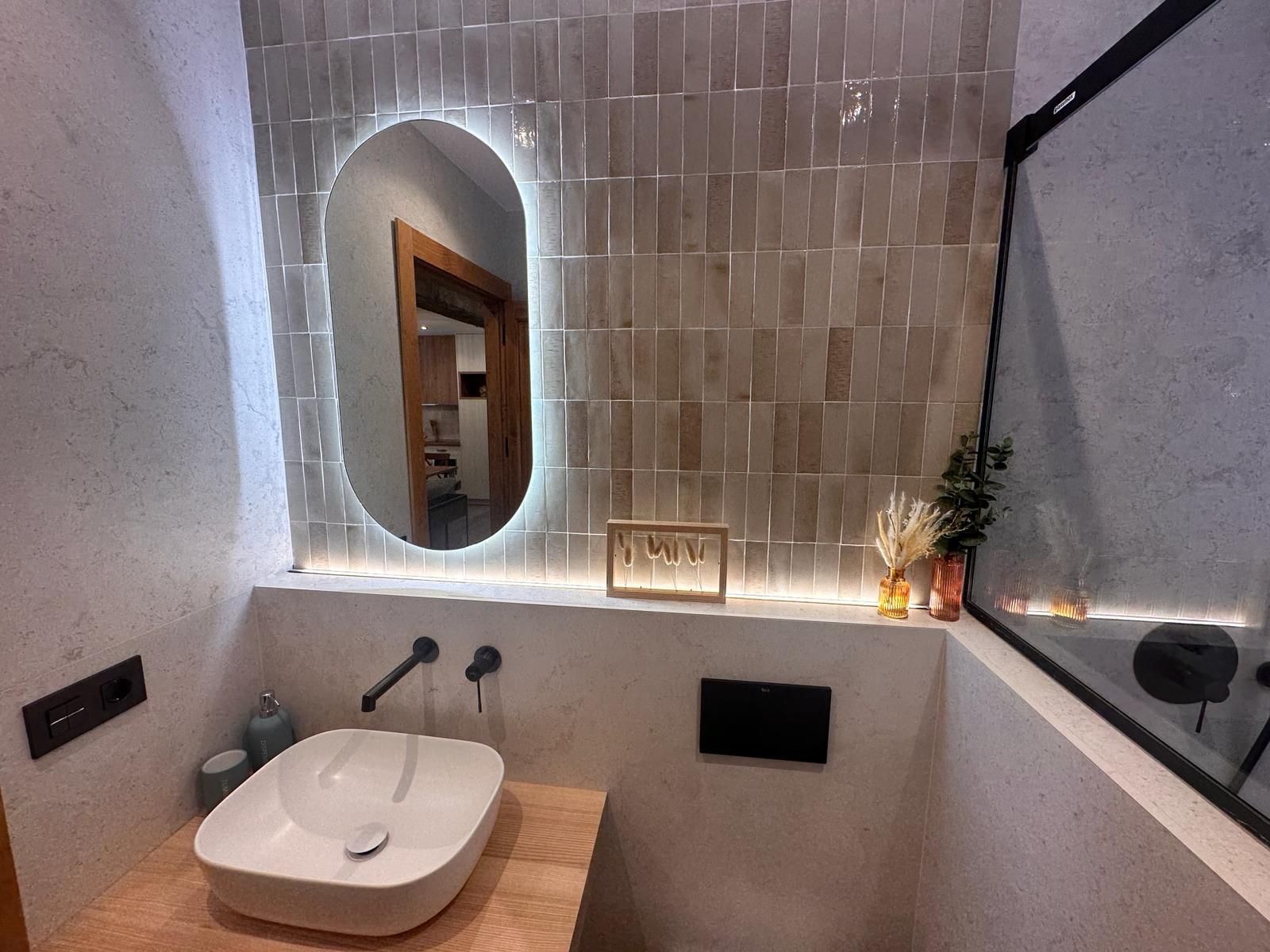 Baño moderno con espejo iluminado y azulejos verticales