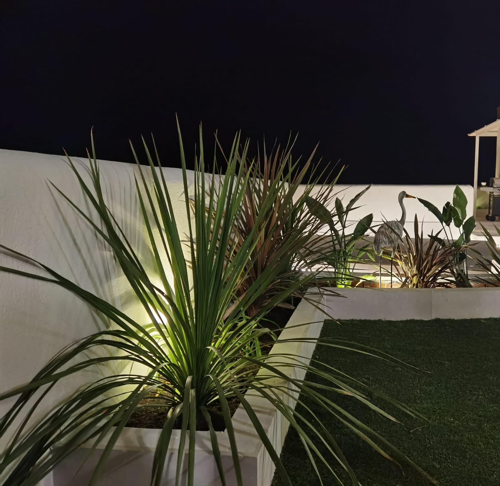 Jardinera de obra exterior revestida en cerámica clara con iluminación nocturna y plantas